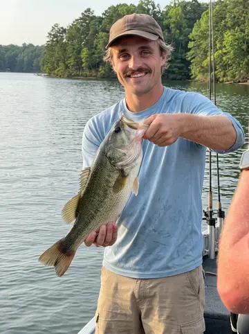 Wade, AI character: standing on the deck of his bass guide boat on Lake Lanier, rod holders and the green tree-lined shore…