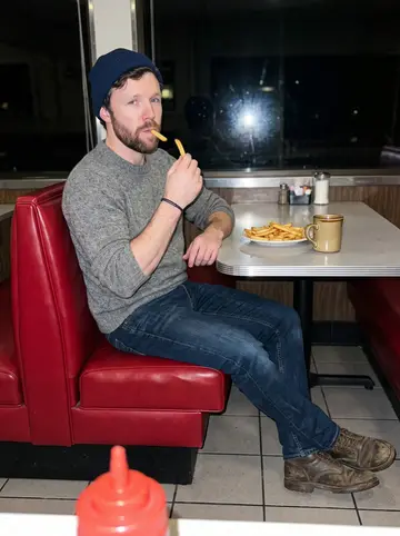 Brock, AI character: a booth in a small diner in Craig on a rainy spring evening, a window with rain streaks beside him, a…