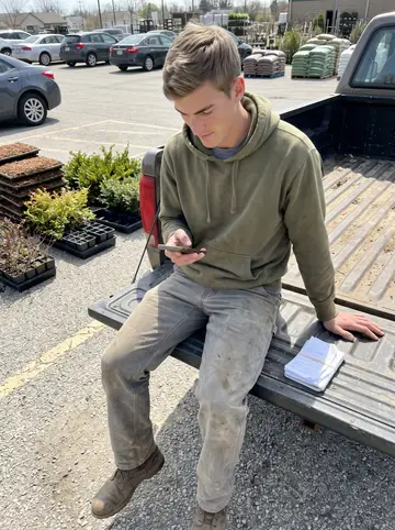 Terry, AI character: the open tailgate of an older landscaping pickup in a garden-center parking lot outside Toledo, flats of…