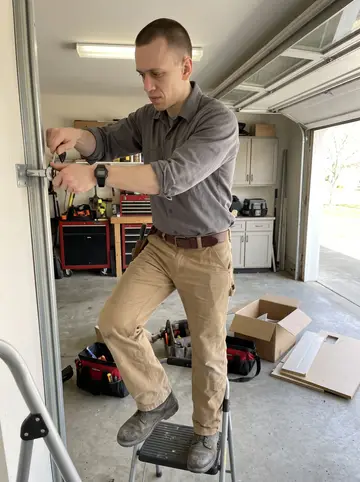 Jared, AI character: inside a customer's open garage in Akron, standing on a short ladder while lining up an overhead door track