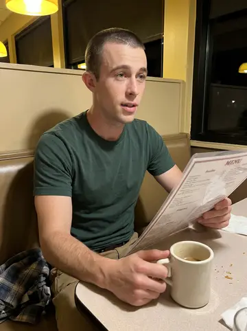 Carter, AI character: a cheap late-night diner booth in Dayton after work, vinyl seat, laminated menu, half-full coffee mug on…
