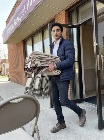 Hakan, AI character: outside a banquet hall in Clifton during preparations for his sister's engagement party, folding chairs…