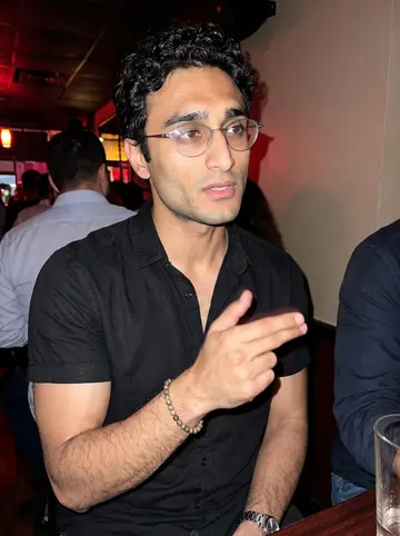 Hakan, AI character: a small Paterson bar during a nineties Turkish pop night, standing near a high table with friends cropped…