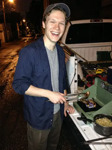 Hendrik, AI character: alley behind his truck after a late service call, camping stove set on the tailgate with brats and sauerkraut