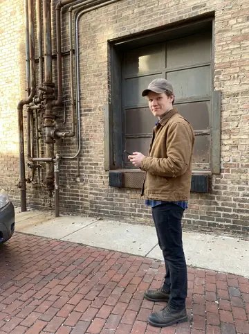 Hendrik, AI character: brick walkway outside an old Milwaukee brewery building, rusted pipework and old loading doors along the wall
