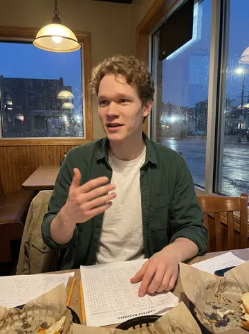 Hendrik, AI character: corner table at a Milwaukee tavern during a fantasy baseball draft, score sheets and half-finished food…