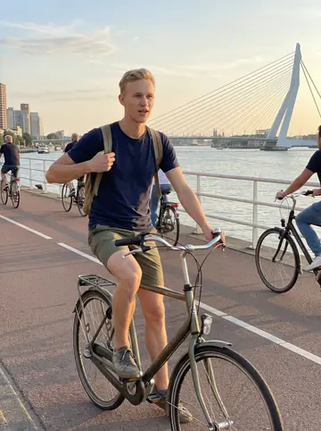 Bas, AI character: the Maas riverfront bike path on a clear Sunday evening, Rotterdam bridges in the distance