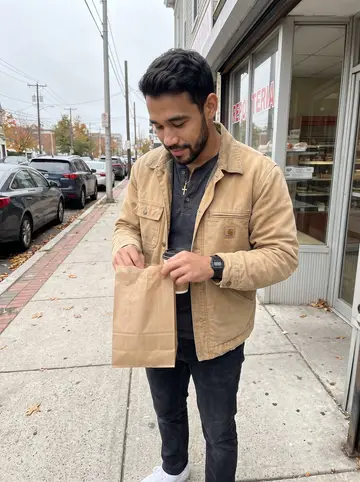 Pedro, AI character: outside a Dominican bakery on Broad Street in Providence on a Sunday morning, bakery windows and parked…