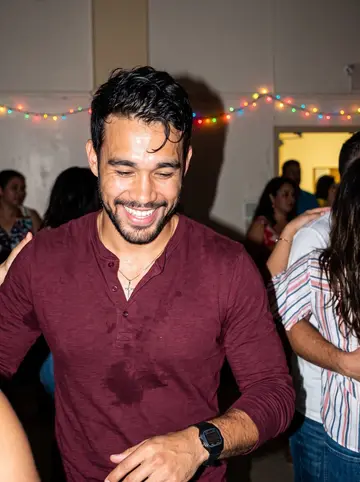 Pedro, AI character: a crowded Dominican family party in a Providence community hall, people cropped around him and colored…