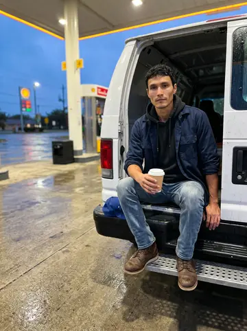 Diarmuid, AI character: under the canopy of a gas station south of San Antonio on the way back from the Medina River, wet pavement…