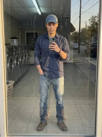 Diarmuid, AI character: dark laundromat window on a quiet San Antonio street, using the glass reflection while waiting for work…