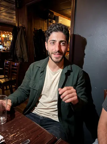 Amílcar, AI character: a crowded Ironbound bar after closing the shop, small table near the wall with friends just out of frame