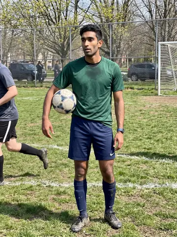 Vikram, AI character: a public soccer field in Pittsburgh on Sunday morning, chain-link fence and budding trees in the background