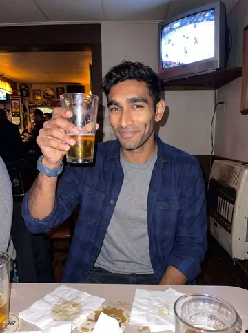 Vikram, AI character: a neighborhood bar in Pittsburgh during a Penguins game, old TV glow and a wall heater behind the table