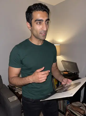 Nabil, AI character: a friend's living room in Dearborn after dinner, old Motown and Fairuz records stacked beside a small…