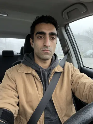 Nabil, AI character: parked in his car before an early dialysis drop-off, Dearborn side street blurred through the windshield