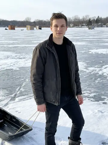 Jon, AI character: a frozen lake outside Eau Claire on a clear winter afternoon, ice shacks and bare trees far behind him