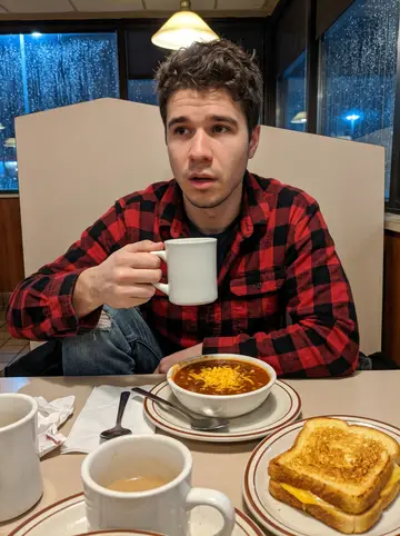 Corey, AI character: a Cincinnati diner booth late after work, a bowl of chili and grilled cheese on the table, rain-dark…