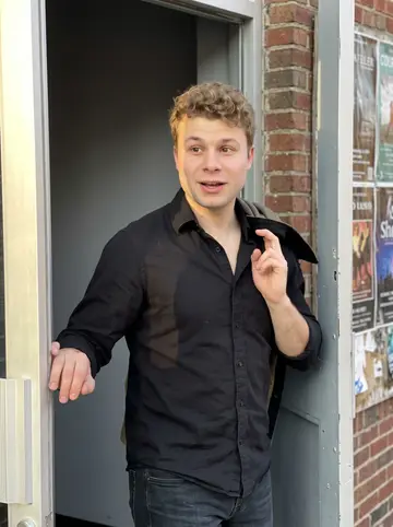 Milo, AI character: outside a small Cleveland rehearsal hall after opera chorus practice, brick wall and stage door behind him