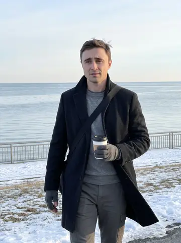 Dawid, AI character: Buffalo waterfront path near sunrise, Lake Erie behind him with patches of snow along the railing