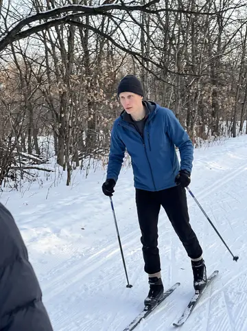 Per, AI character: a groomed cross-country ski trail at Theodore Wirth Park in Minneapolis, bare winter trees and packed snow…
