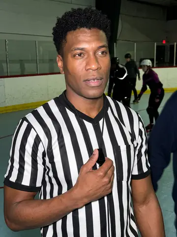 Rodney, AI character: a crowded Detroit roller rink during a Saturday roller derby bout, painted rink boards and skaters blurred…