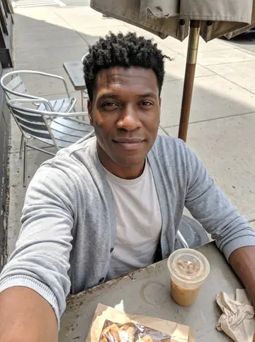 Rodney, AI character: a small cafe patio in Detroit on his rare slow Sunday, iced coffee and a paper bag of test pastries on the…
