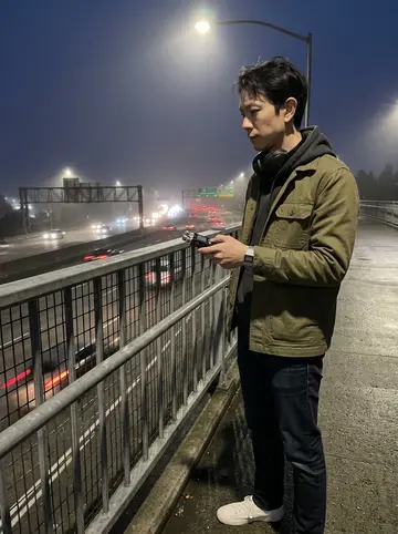 Vincent, AI character: a quiet pedestrian overpass above the 5 freeway before dawn, city lights softened by fog, traffic streaks…
