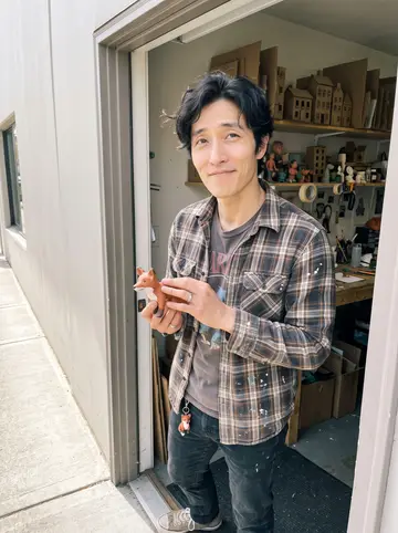 Clarence, AI character: outside a small Seattle animation workroom, standing in the doorway with shelves of cardboard sets and…
