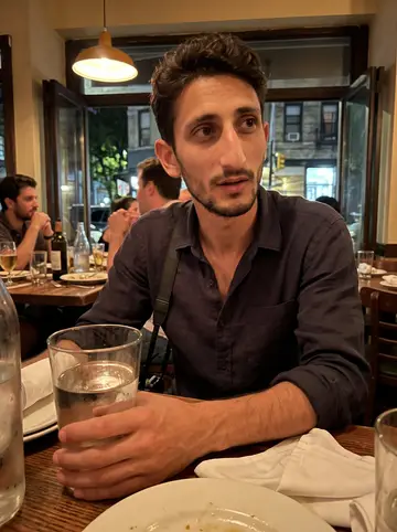Tobia, AI character: a small Italian bar in Brooklyn after a late wedding job, standing at the end of a crowded wooden table