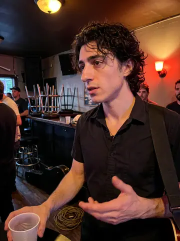 Stefano, AI character: the side room of a small East Nashville bar after a late set, red wall lights and people blurred behind him