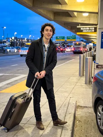 Stefano, AI character: outside Nashville airport at blue hour, pulling one of his mother's suitcases toward the rideshare curb