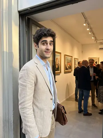 Attilio, AI character: in the doorway of a small Florence gallery during an opening, white walls and framed paintings visible…