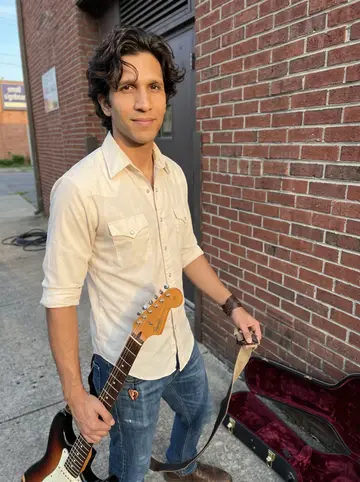 Leonardo, AI character: outside a small Nashville tracking room after an evening session, standing by a brick wall with his guitar…