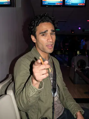 Faisal, AI character: a cheap Rogers Park bowling alley on a Thursday night, score screens and plastic seats behind him