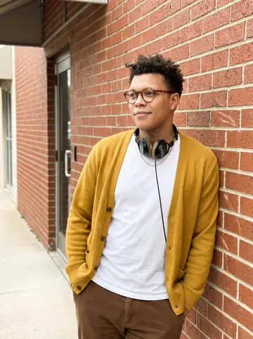 Reuben, AI character: outside a small Austin audio office, leaning against the brick wall by a side door after a daytime…