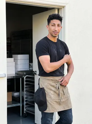 Blair, AI character: outside the church kitchen side door in Oakland just after sunrise, prep tables and stacked cake boxes…