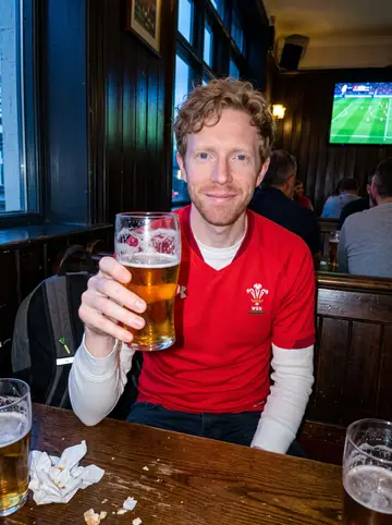 Gareth, AI character: a crowded Cardiff pub during a Wales rugby match, TV glow and dark wood wall behind him