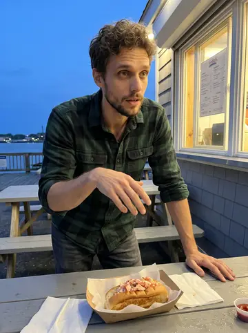 Tom, AI character: outside a lobster-roll shack near the Portland waterfront, picnic tables and a takeout window glowing…