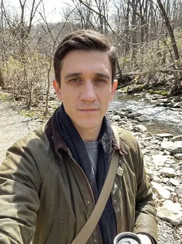 Alexei, AI character: the creek path in Frick Park during his regular thermos walk, bare spring branches and running water…