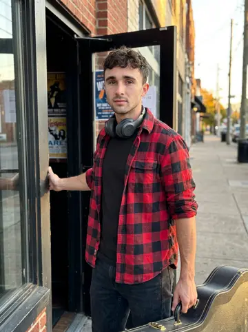 Tiernan, AI character: outside a small bar on Eighth Avenue in Nashville before Tuesday jam night, brick wall and guitar cases…