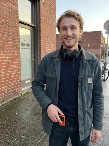 Ludvig, AI character: outside the small game-audio office after work, brick wall and wet Bergen-like street behind him
