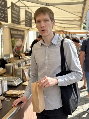 Pascal, AI character: a Saturday tea stall at the Leipzig market, loose tea tins and paper bags on the counter