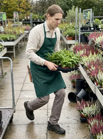Tijmen, AI character: between the outdoor plant tables at the garden centre, wet paving stones and rows of potted heathers…