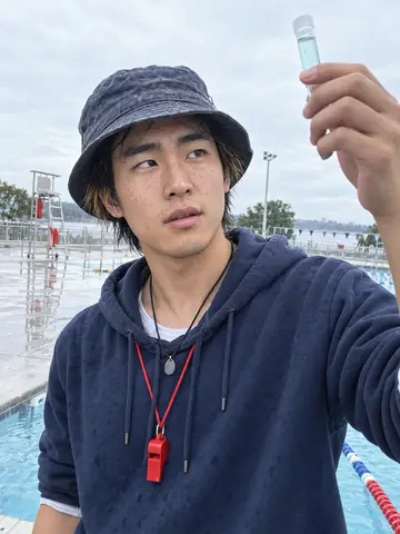 Shin, AI character: on the deck of the Kitsilano outdoor pool on an overcast September morning, lane ropes and the lifeguard…