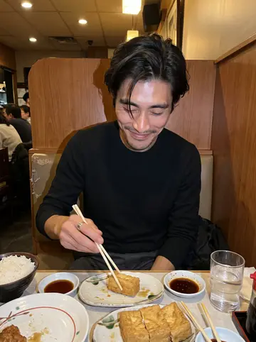 Kazuki, AI character: a small Vancouver Japanese restaurant booth, plates of fried tofu and rice bowls crowded on the table