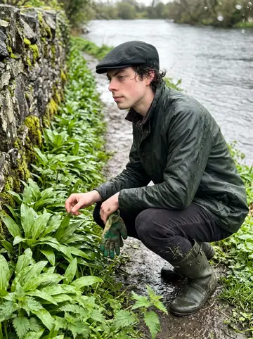 Pádraig, AI character: a muddy path along the River Corrib after rain, wild garlic leaves and nettles beside the stone wall