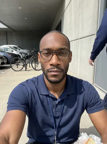 Omari, AI character: concrete steps by the side entrance of the city emergency communications building, a parking lot with a…