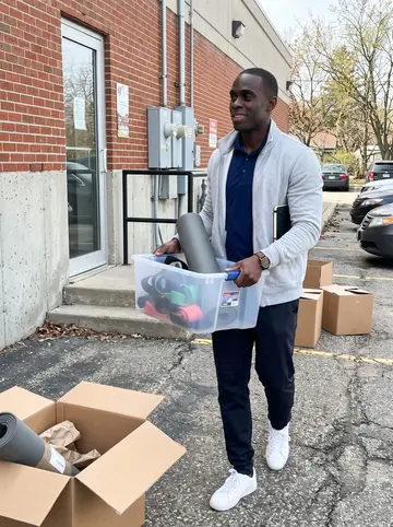 Junior, AI character: outside the closed outpatient clinic in suburban Detroit, by the back entrance and a stack of packed boxes