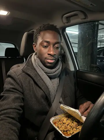 Ifeanyi, AI character: his apartment kitchen on a cold night, a pot of egusi soup on the stove and a phone propped open to a…